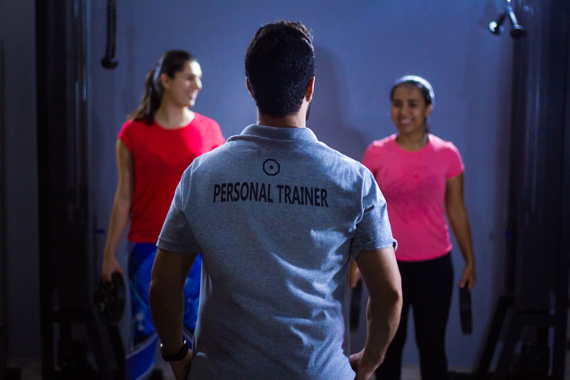 Coach sportif expliquant une série de musculation dans une salle de sport sombre